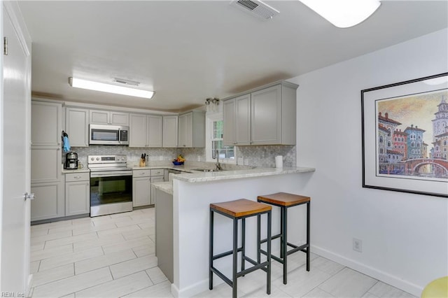 kitchen with visible vents, a peninsula, backsplash, gray cabinetry, and stainless steel appliances