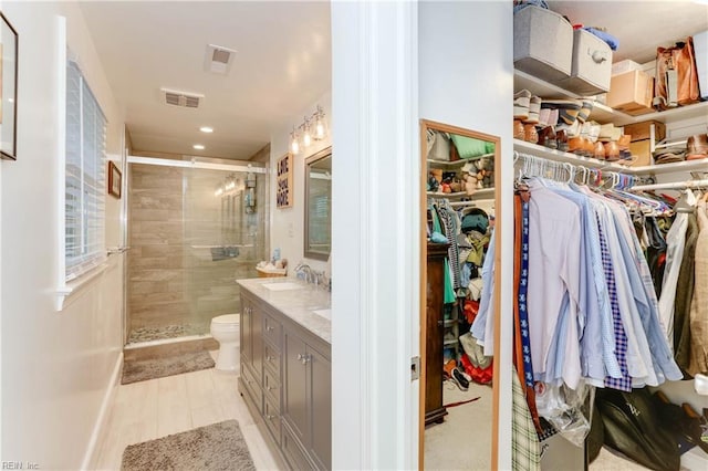 bathroom with a walk in closet, visible vents, a shower stall, vanity, and toilet