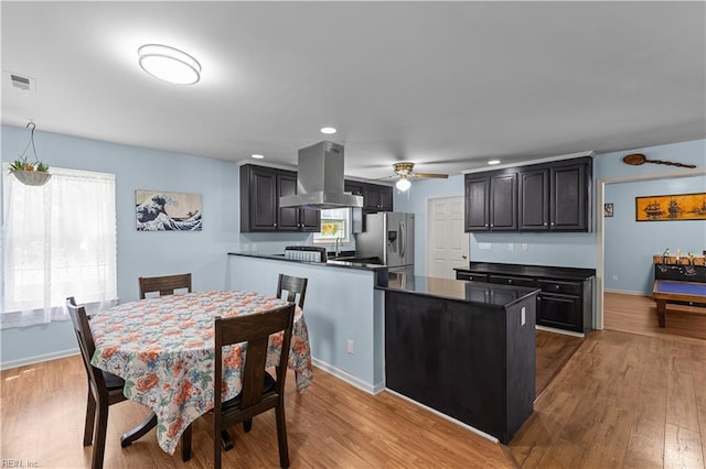 kitchen featuring visible vents, wood finished floors, dark countertops, stainless steel fridge, and island exhaust hood
