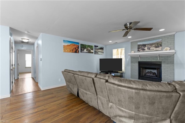 living room with baseboards, a brick fireplace, ceiling fan, and wood finished floors