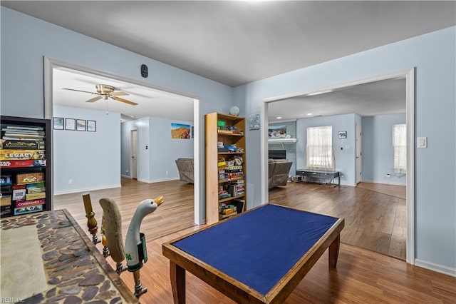 game room with baseboards, ceiling fan, a brick fireplace, and wood finished floors
