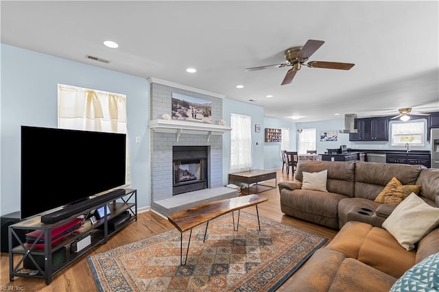 living room with a fireplace, a ceiling fan, wood finished floors, and visible vents