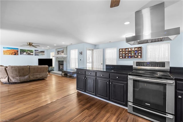 kitchen with wall chimney range hood, dark countertops, electric stove, a ceiling fan, and dark wood-style floors