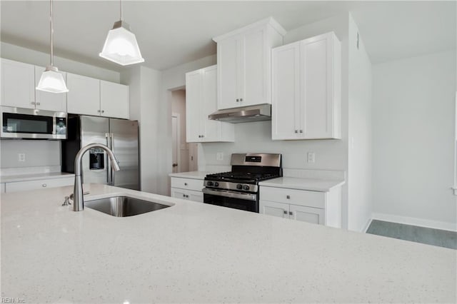 kitchen featuring pendant lighting, white cabinetry, under cabinet range hood, a sink, and appliances with stainless steel finishes