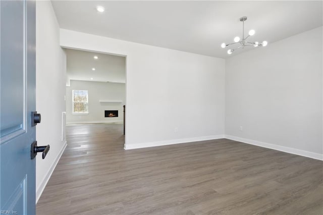 empty room featuring baseboards, recessed lighting, wood finished floors, and a notable chandelier