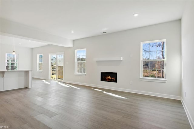 unfurnished living room featuring a lit fireplace, a wealth of natural light, wood finished floors, and visible vents