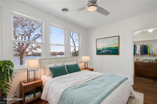 bedroom featuring a walk in closet, visible vents, wood finished floors, a closet, and a water view