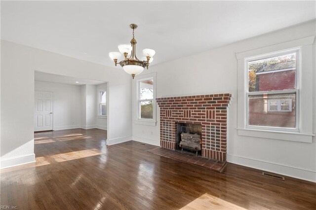 unfurnished living room with baseboards, a notable chandelier, visible vents, and wood finished floors