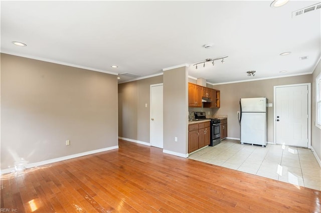 kitchen featuring brown cabinetry, baseboards, stainless steel gas range, freestanding refrigerator, and ornamental molding
