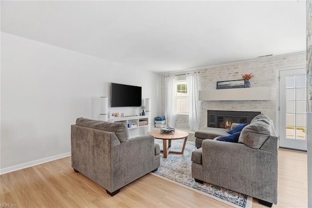 living area with a brick fireplace, baseboards, and light wood-type flooring