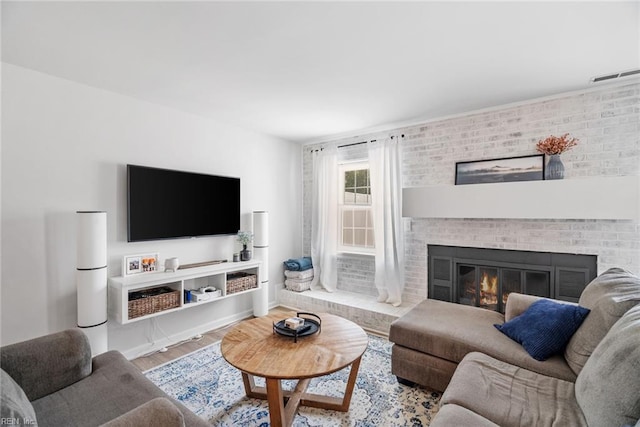 living area with visible vents, a brick fireplace, and wood finished floors