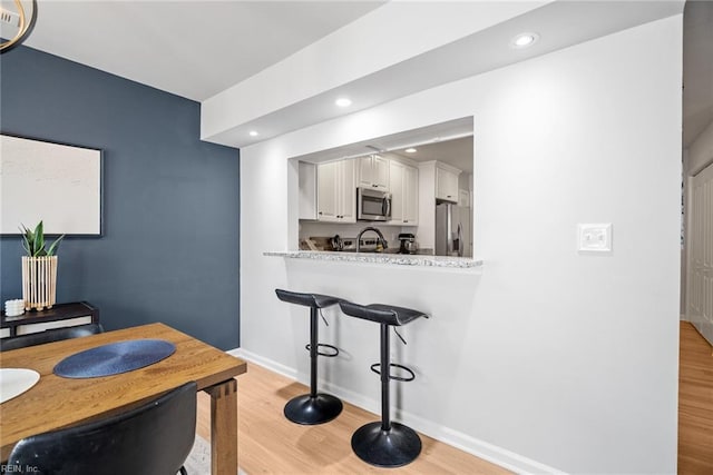 kitchen with appliances with stainless steel finishes, a kitchen bar, light wood-style flooring, and white cabinetry