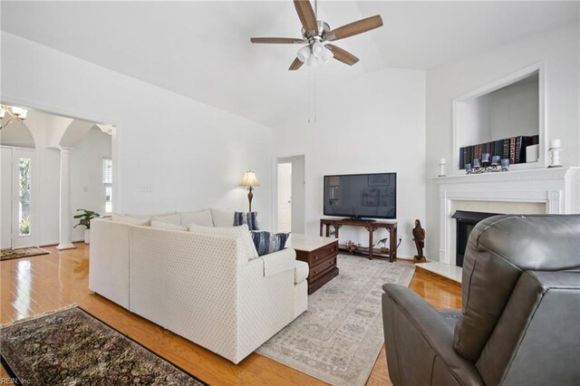 living area featuring light wood finished floors, a ceiling fan, a fireplace with flush hearth, ornate columns, and vaulted ceiling