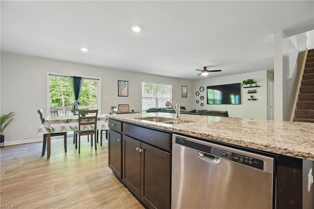 kitchen featuring stainless steel dishwasher, light wood-type flooring, a sink, light stone counters, and open floor plan