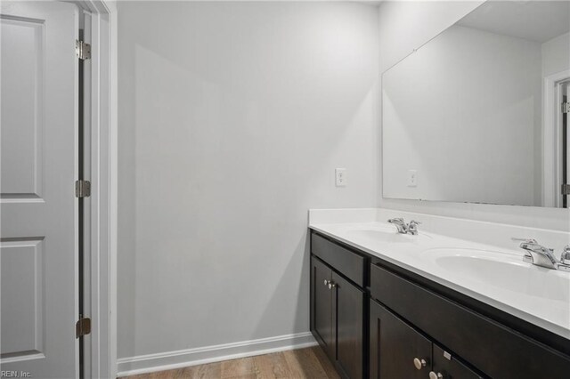 bathroom featuring double vanity, baseboards, a sink, and wood finished floors
