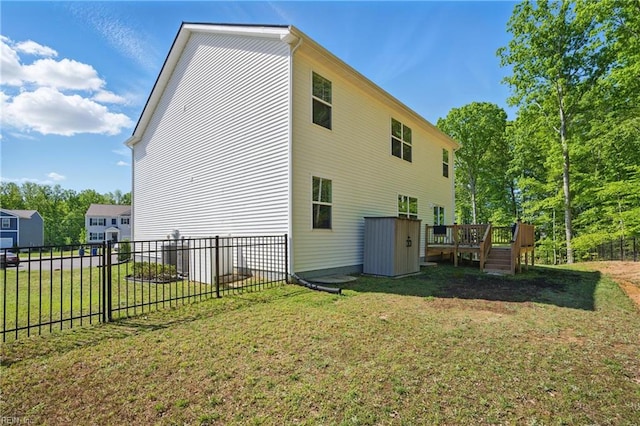 back of house featuring fence, a storage unit, a deck, an outdoor structure, and a yard
