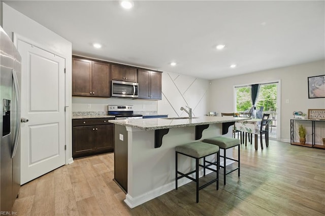 kitchen featuring light wood-style flooring, dark brown cabinetry, a breakfast bar, and stainless steel appliances