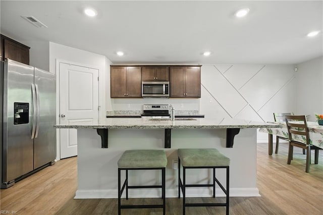 kitchen with light wood finished floors, a breakfast bar, dark brown cabinets, and stainless steel appliances