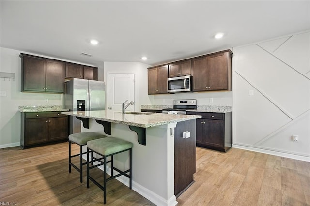 kitchen with dark brown cabinets, light wood-style floors, a kitchen breakfast bar, a sink, and stainless steel appliances