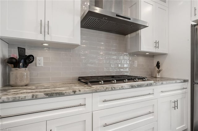 kitchen with tasteful backsplash, white cabinets, wall chimney range hood, and stainless steel gas stovetop