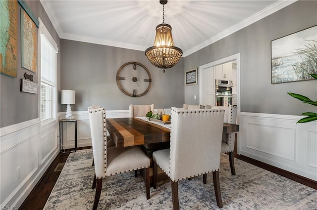 dining room with wainscoting, dark wood-style flooring, an inviting chandelier, and ornamental molding