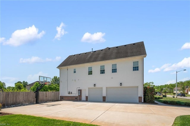 rear view of property featuring a garage, concrete driveway, fence, brick siding, and basketball hoop