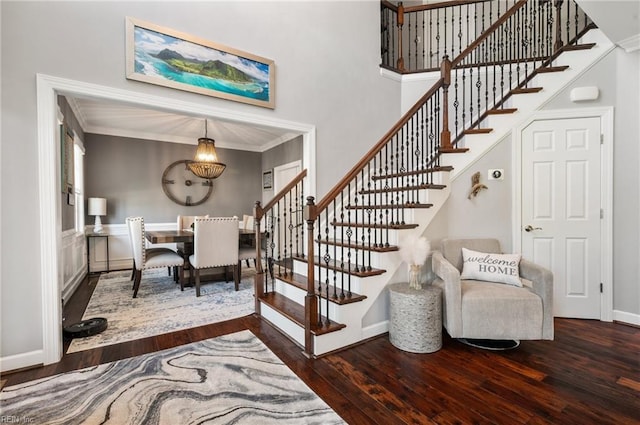 staircase with ornamental molding, a high ceiling, wood finished floors, and a chandelier