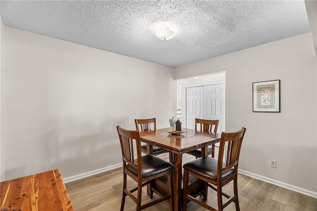 dining room featuring a textured ceiling, baseboards, and light wood-type flooring