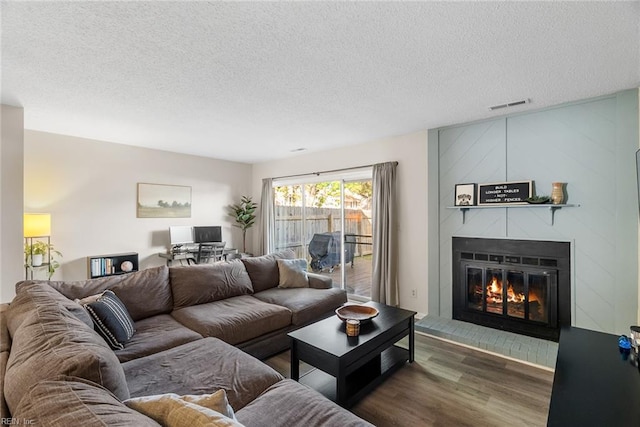 living room with visible vents, a textured ceiling, dark wood-type flooring, and a large fireplace