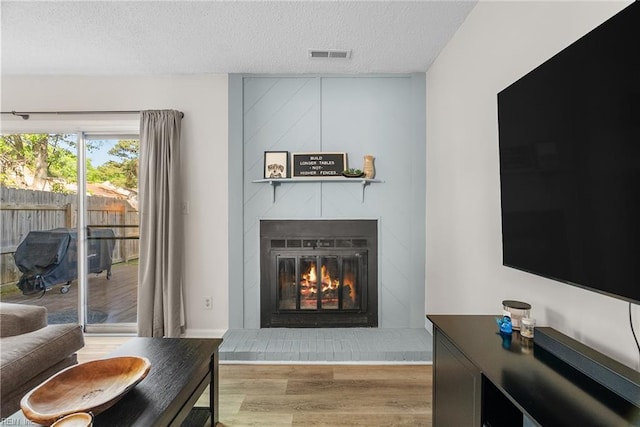 living area featuring a glass covered fireplace, a textured ceiling, wood finished floors, and visible vents