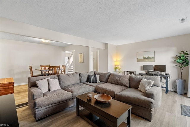 living area with visible vents, stairs, a textured ceiling, and wood finished floors