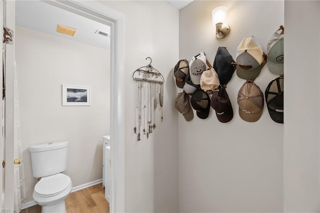 half bath featuring toilet, baseboards, visible vents, and wood finished floors