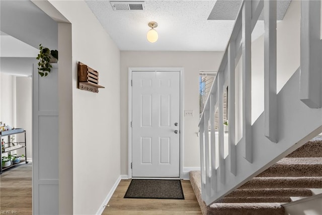 foyer entrance with visible vents, baseboards, stairway, light wood-type flooring, and a textured ceiling