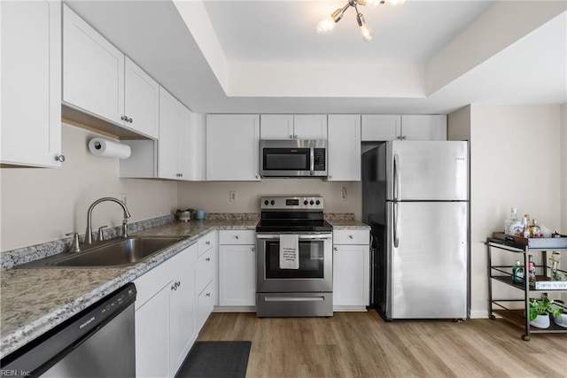 kitchen featuring appliances with stainless steel finishes, a sink, a raised ceiling, white cabinetry, and light wood-type flooring
