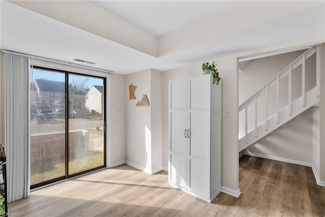 interior space featuring baseboards, wood finished floors, visible vents, and stairway