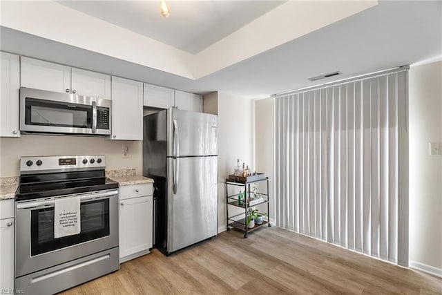 kitchen with light stone counters, stainless steel appliances, light wood-style flooring, and white cabinetry