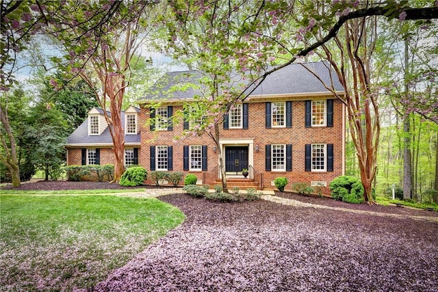 colonial-style house featuring brick siding and a front yard