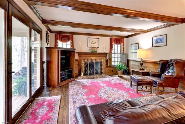 living area featuring a brick fireplace, wood finished floors, beamed ceiling, visible vents, and ornamental molding