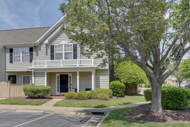 view of front of home featuring a porch, uncovered parking, fence, and a balcony