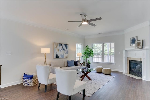 living area featuring a tiled fireplace, ornamental molding, a ceiling fan, and dark wood-type flooring