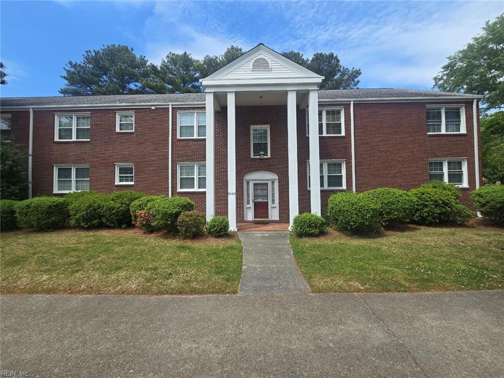 greek revival inspired property featuring a front lawn and brick siding