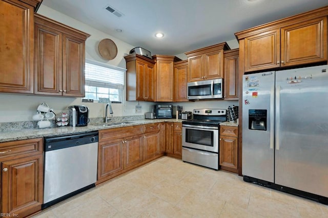 kitchen with appliances with stainless steel finishes, brown cabinetry, and a sink