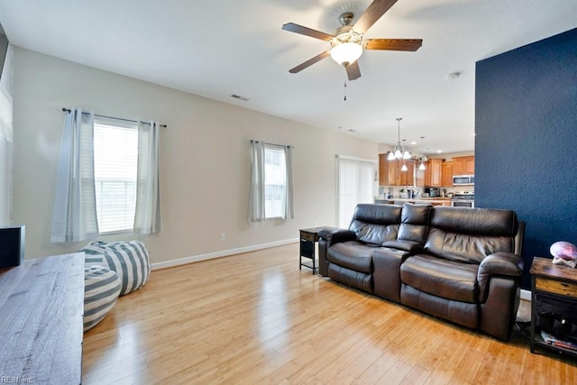 living room featuring light wood-type flooring, baseboards, ceiling fan with notable chandelier, and visible vents