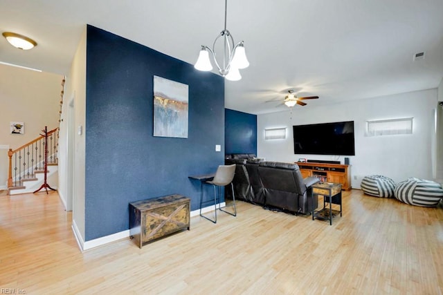 living area with baseboards, ceiling fan with notable chandelier, light wood finished floors, and stairs