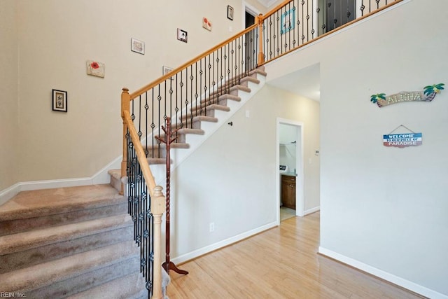 stairway featuring baseboards, wood finished floors, and a towering ceiling