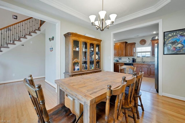 dining area with crown molding, an inviting chandelier, baseboards, light wood-type flooring, and a tray ceiling