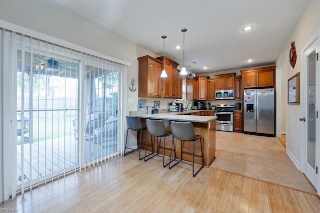 kitchen featuring brown cabinetry, appliances with stainless steel finishes, hanging light fixtures, a peninsula, and a breakfast bar
