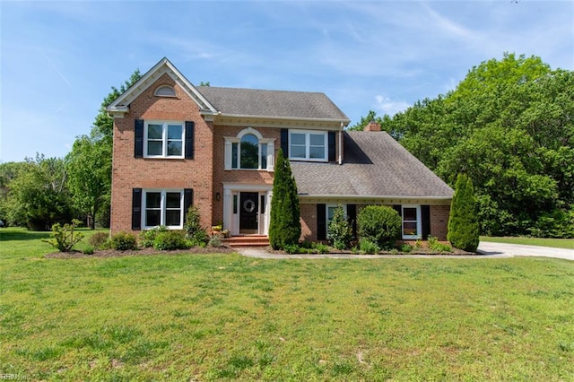 view of front of house featuring brick siding, a front lawn, and a chimney