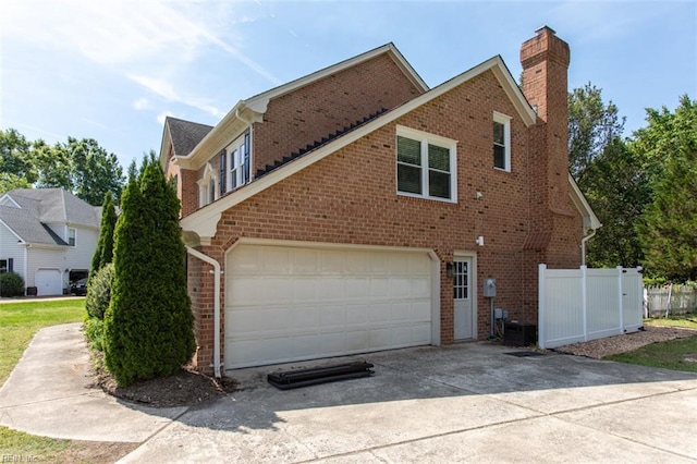 view of home's exterior with brick siding, a garage, a chimney, and concrete driveway