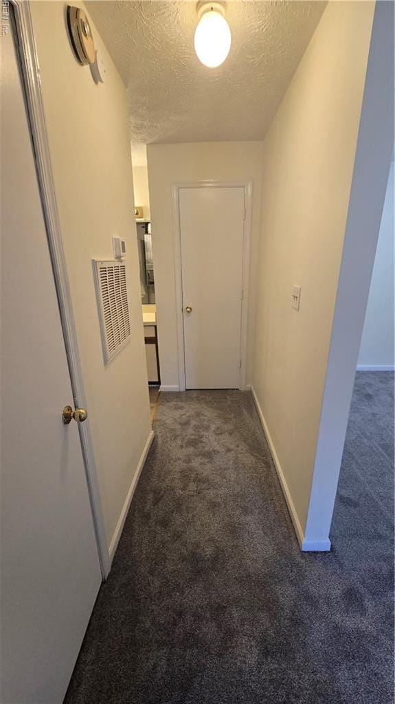 hallway featuring baseboards, a textured ceiling, and carpet